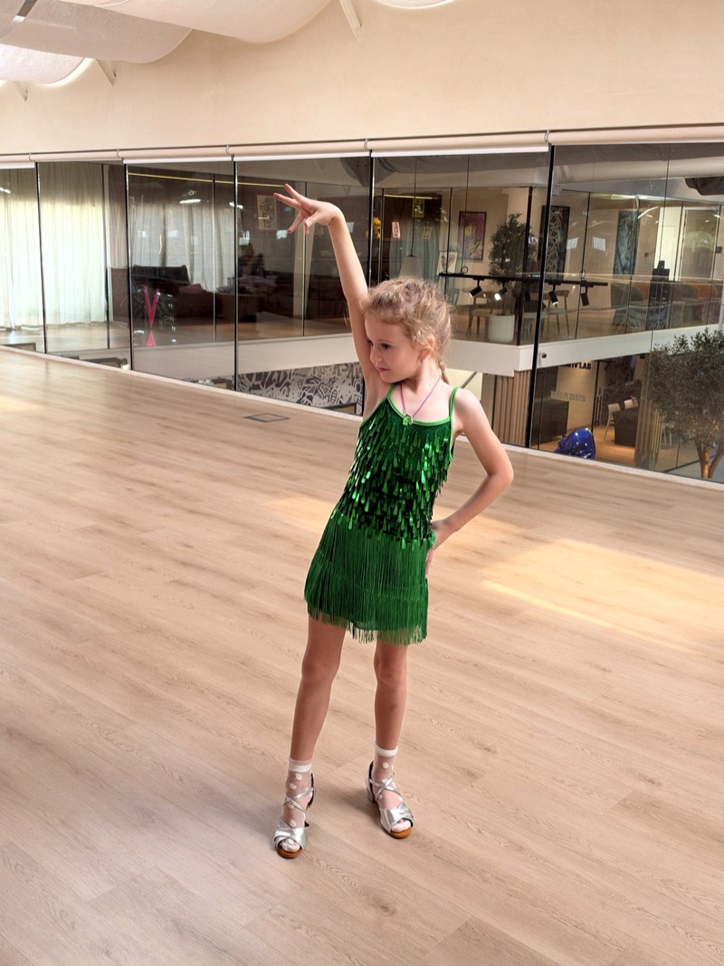 A girl in a green fringe Latin dress posing in a dance hall
